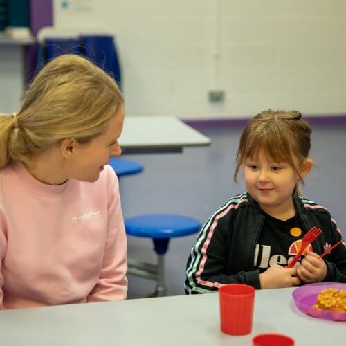 A child eating breakfast with her teacher.