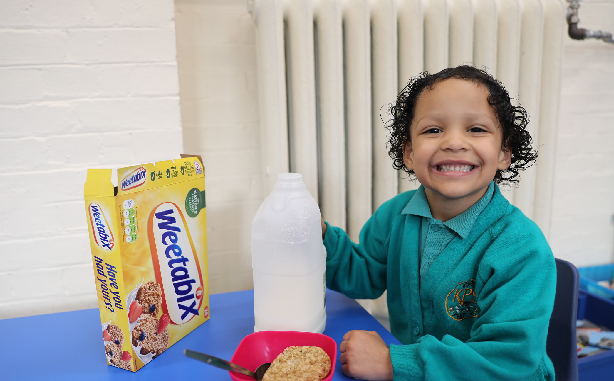 A young boy smiling happily in school uniform, with his milk and Weetabix