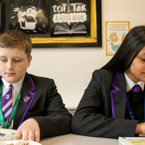 A photo of two teens in school uniforms reading their textbook.