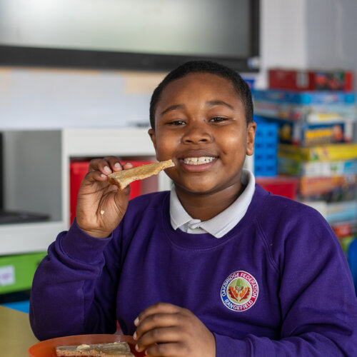 A young boy eating toast and smiling to camera