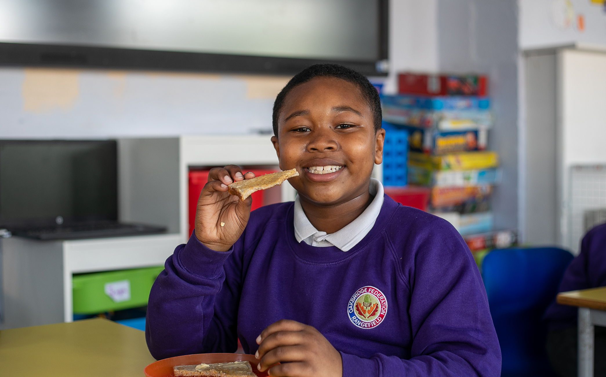 A young boy eating toast and smiling to camera