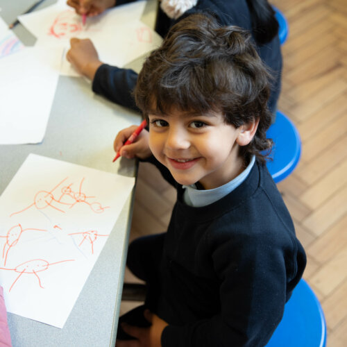 Image of a child drawing, looking at the camera smiling
