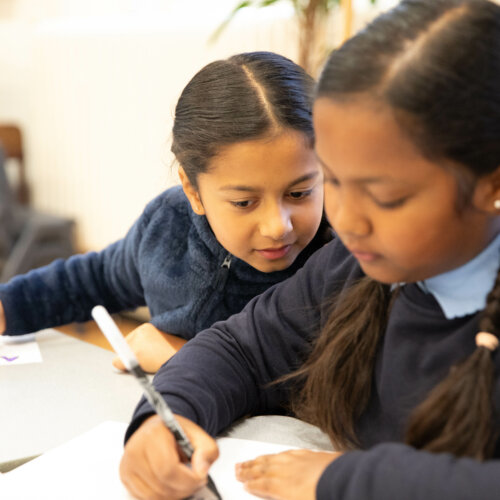 Two school children writing at a desk.