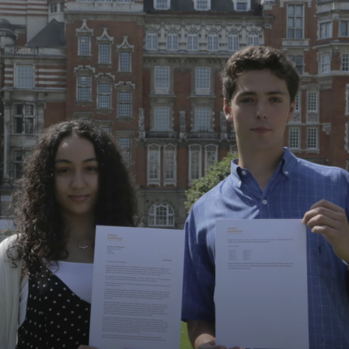 Two youth campaigners in front of a grand building holding up a letter from Magic Breakfast