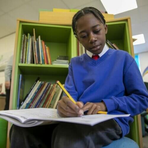 Photo of boy in blue uniform in a library writing in a textbook.