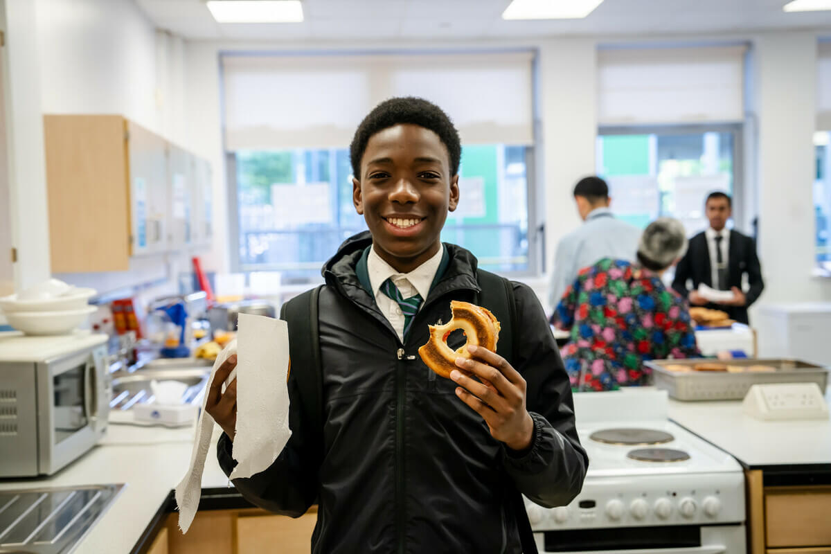 Secondary school student smiles as they hold their bagel in the school cooking area