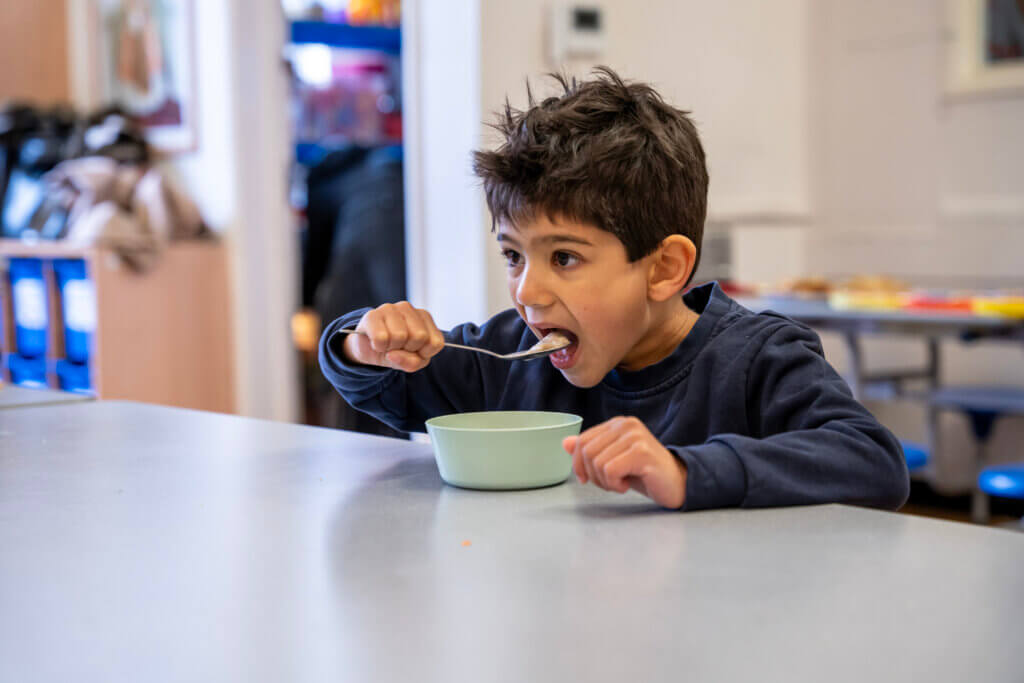 A primary school pupil lifts a spoonful of his Magic Breakfast - which today is cereal - to his mouth as he sits at his school desk to eat