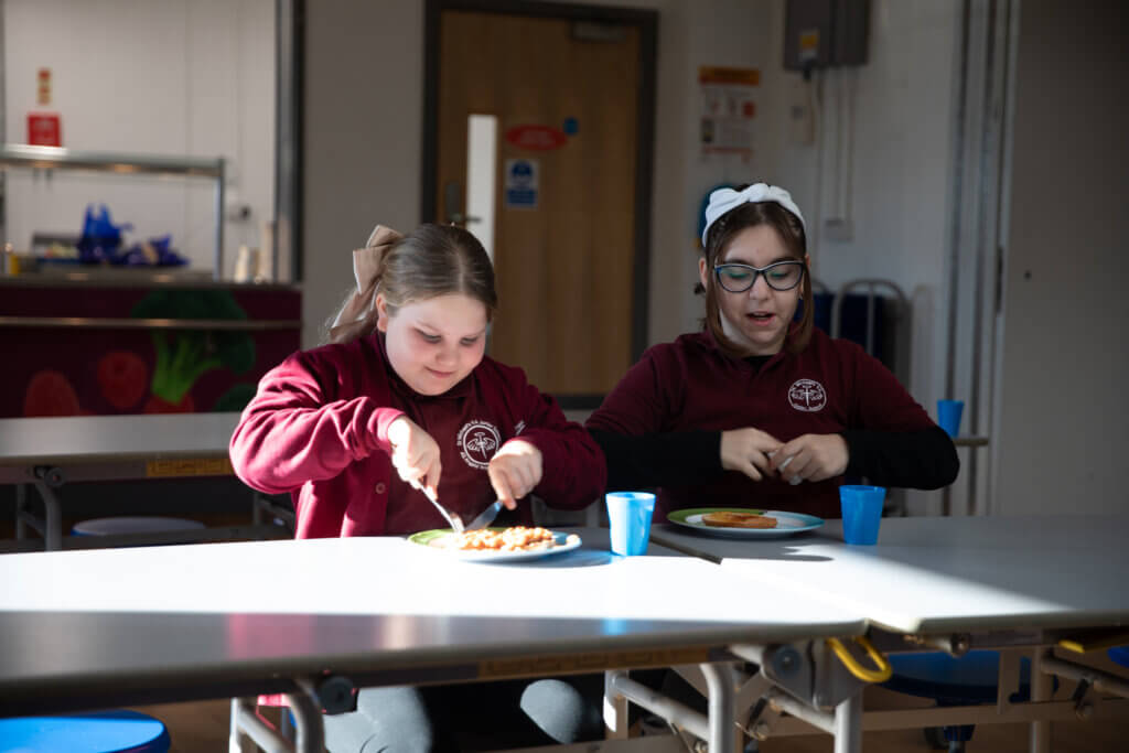 Two primary school children chat happily as they sit together to eat their school breakfast