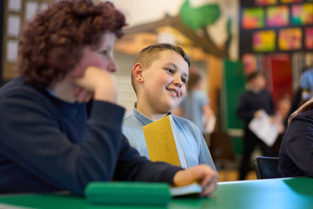 Smiling primary school students look happily at something out of view as they sit at their desks, ready to learn