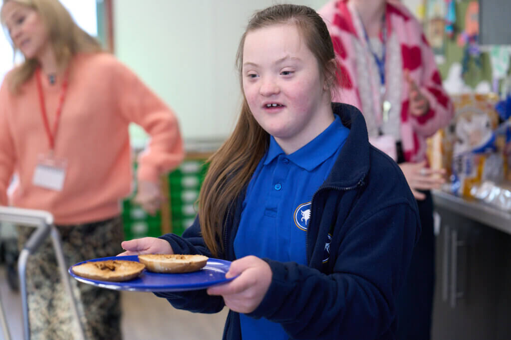 A student at a Magic Breakfast SEN partner school carries her plate of bagels with a smile