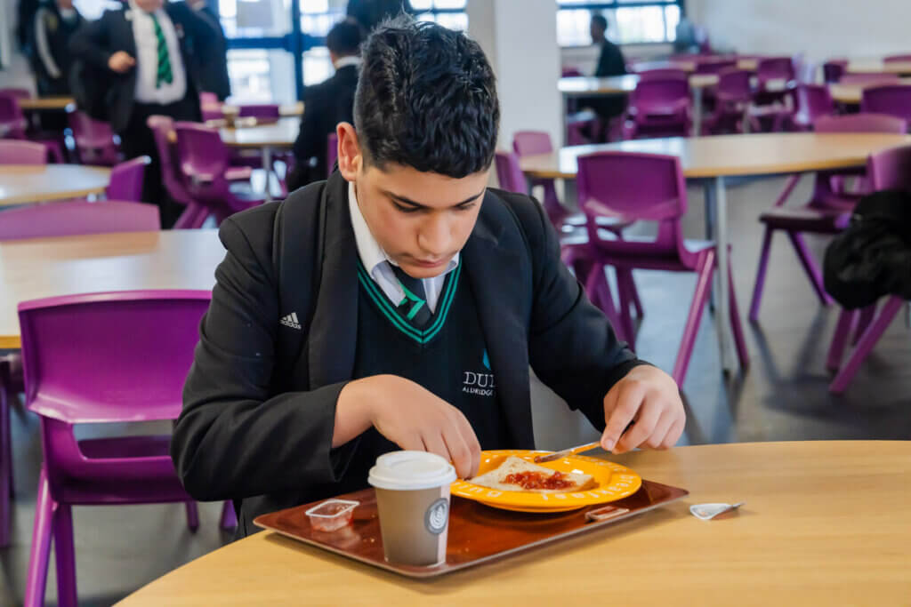 Secondary pupils sits and enjoys breakfast in a school canteen
