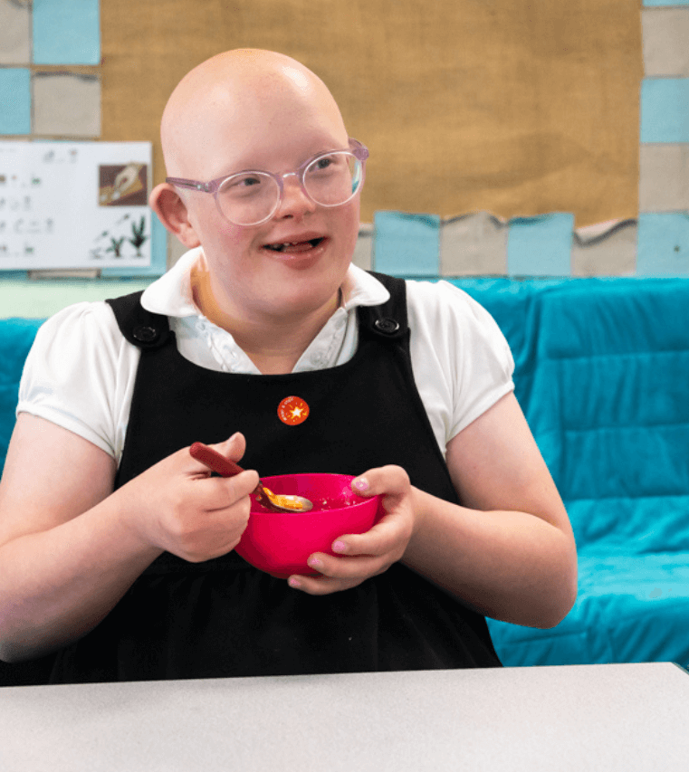 An SEND learner smiles as she eats her morning cereal