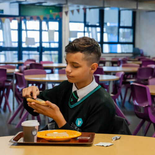 A secondary school student butters their toast in the school hub
