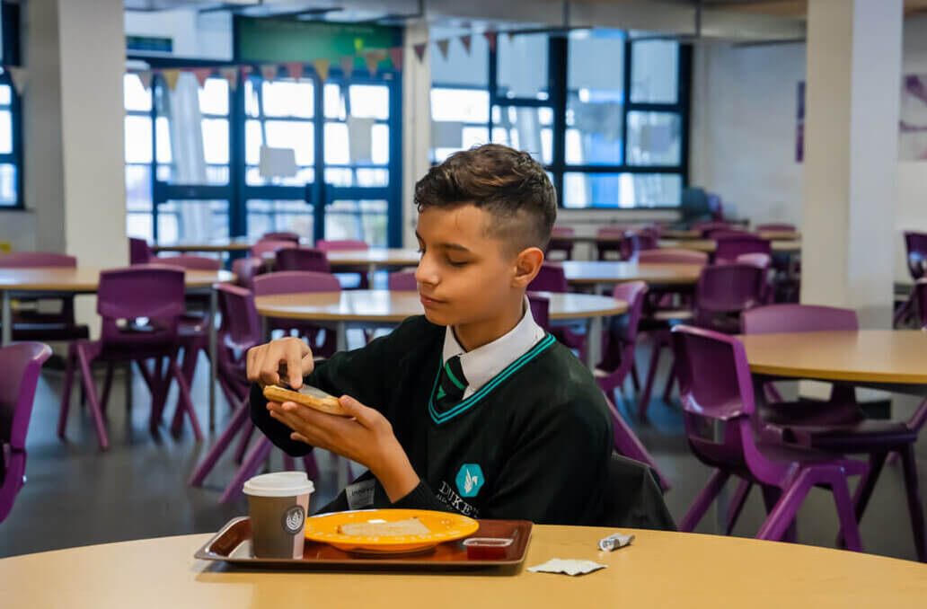 A secondary school student butters their toast in the school hub
