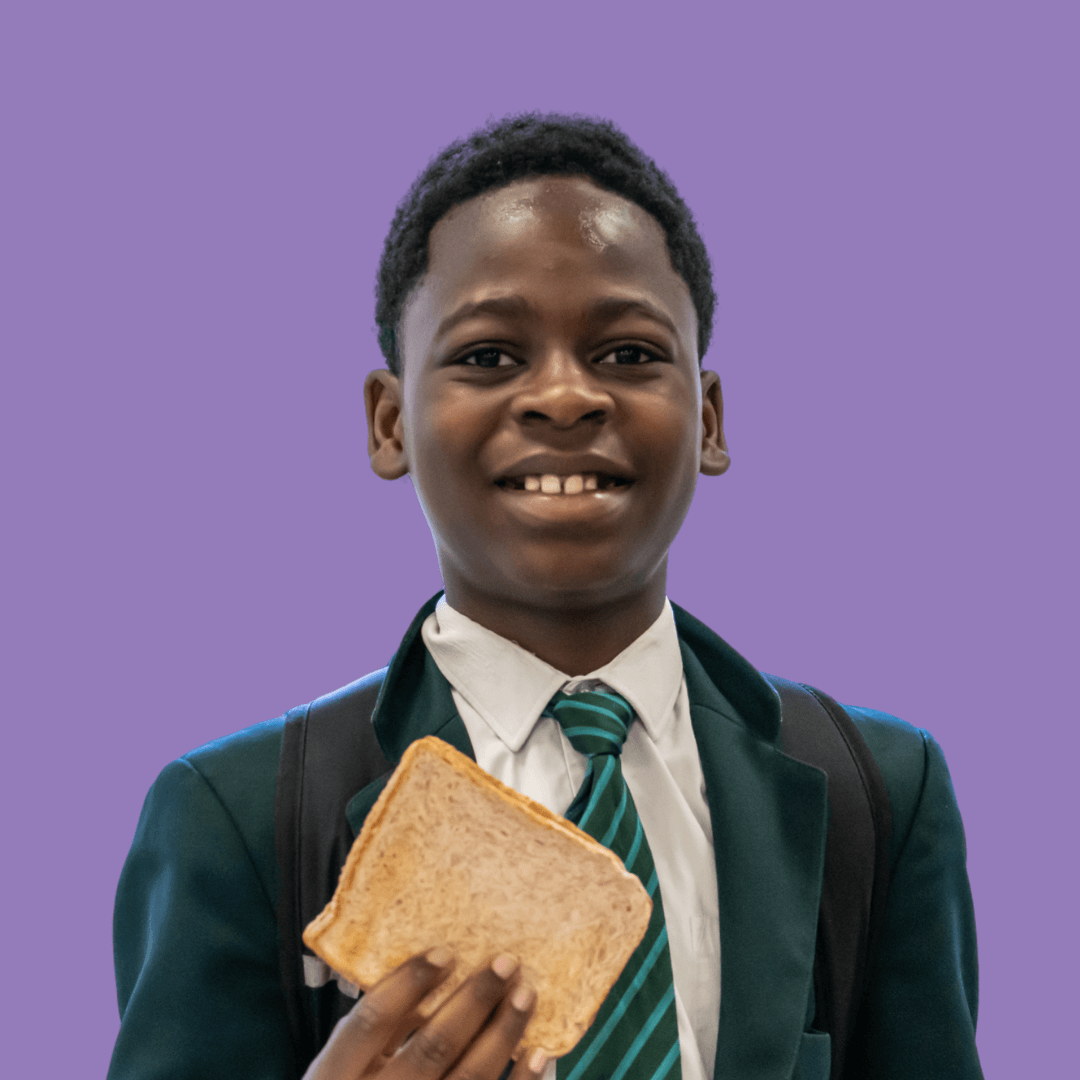 A secondary school student smiles at the camera as they hold their piece of toast up