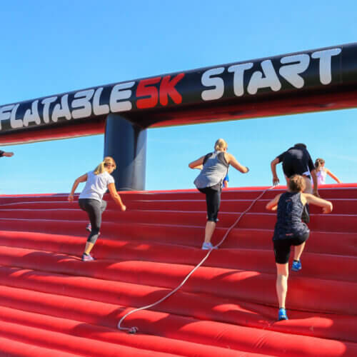 A photo of a group of adults doing an obstacle course and running up an inflatable as part of a 5k.